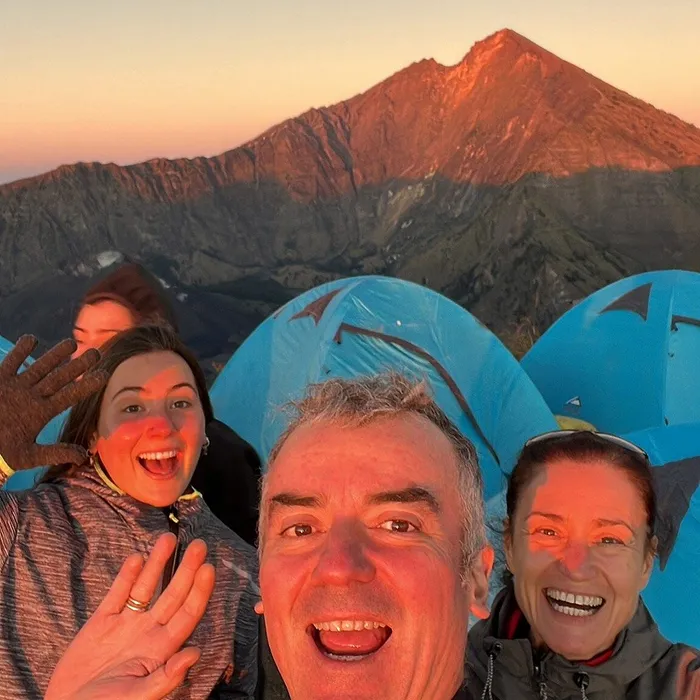 Hiker celebrating at the mount rinjani summit with panoramic views behind